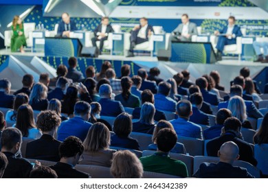 Large business conference with a panel of speakers and a diverse audience in attendance, focusing on various topics and discussions. - Powered by Shutterstock