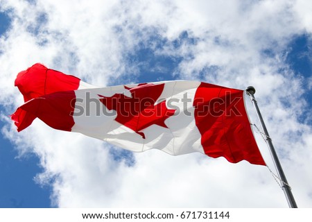 A large Canadian flag flies against a partly cloudy sky.