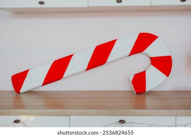 A large candy cane made of red and white fabric rests on a wooden surface. This festive decoration adds a joyful touch, perfect for holiday celebrations and seasonal decor.