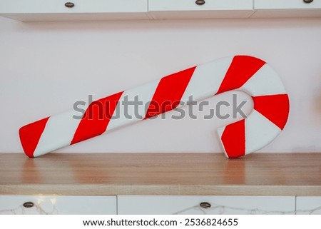 A large candy cane made of red and white fabric rests on a wooden surface. This festive decoration adds a joyful touch, perfect for holiday celebrations and seasonal decor.