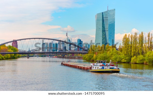 Large Cargo barge moving along the Main River\
with in the background beautiful view of Frankfurt am Main skyline\
- Frankfurt, Germany