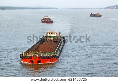 Large cargo barges transporting iron ore mined in hinterland to the main harbor for loading into big ships for exporting, along Mandovi River in Goa, India