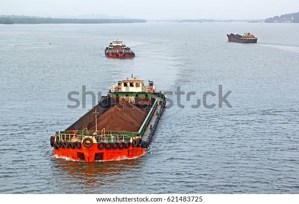 Large cargo barges transporting iron\
ore mined in hinterland to the main harbor for loading into big\
ships for exporting, along Mandovi River in Goa,\
India