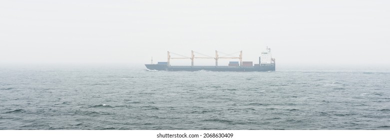 Large Cargo Container Crane Ship Sailing In An Open Sea. Fog, Storm, Rough Weather. Freight Transportation, Nautical Vessel, Logistics, Global Communications, Economy, Industry, Worldwide Shipping