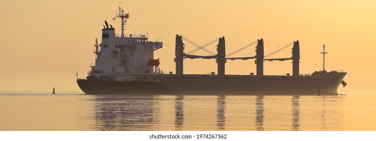 Large cargo crane ship sailing in an open sea at sunset. Golden sunlight. Freight transportation, nautical vessel, logistics, global communications, economy, business, industry, worldwide shipping