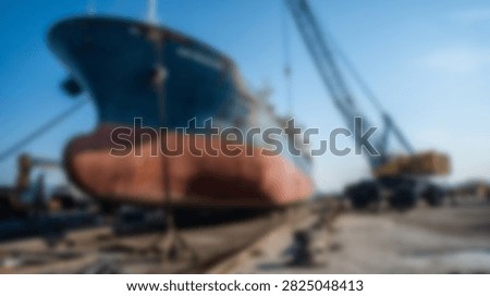 A large cargo ship is positioned in a dry dock for maintenance and repair work, with industrial cranes visible in the background under a clear blue sky.