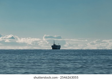 A large cargo ship sailing into the open sea under a serene blue sky with soft clouds. The calm water and distant horizon create a peaceful marine landscape - Powered by Shutterstock