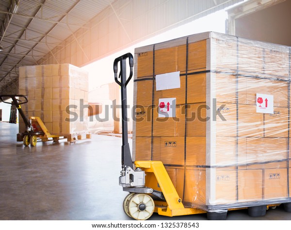 Large cargo\
shipment pallets. Hand pallet truck with stacked cardboard boxes\
wrapping plastic on pallet at warehouse dock. warehouse industry\
freight, logistics and transport.\

