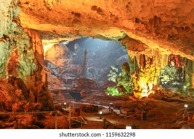 A large cave inside a limestone mountain in Halong Bay, Vietnam with stalagmite formations and sunlight peeking through the end. 