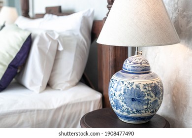 a large ceramic lamp with blue patterns on a white background and a lampshade stands on a wooden bedside table in the bedroom