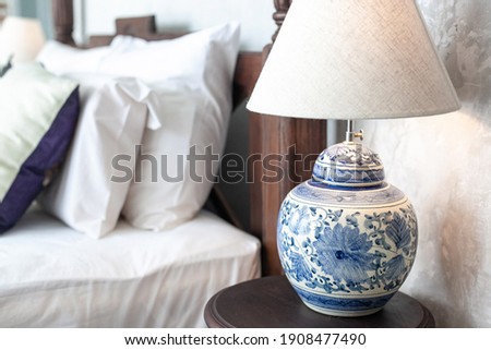 a large ceramic lamp with blue patterns on a white background and a lampshade stands on a wooden bedside table in the bedroom