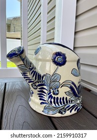 A Large, Ceramic, Watering Can That Is Sitting On A Composite Wood Deck In A Suburban Backyard.