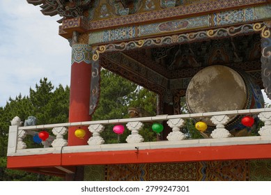 Large ceremonial drum displayed inside a traditional pavilion at Yakcheonsa Temple in Jeju, South Korea. The image documents Buddhist religious architecture and ritual culture. Small Korean characters are present on decorative lanterns but are not legible at this image size.