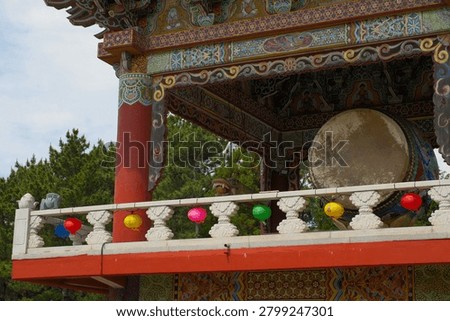 Large ceremonial drum displayed inside a traditional pavilion at Yakcheonsa Temple in Jeju, South Korea. The image documents Buddhist religious architecture and ritual culture. Small Korean characters are present on decorative lanterns but are not legible at this image size.