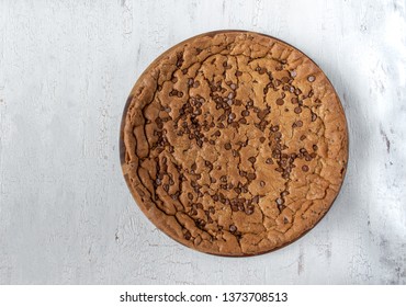 large chocolate chip cookie cake on rustic white background flat lay