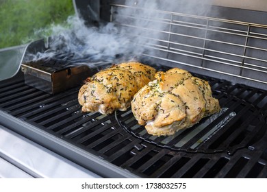 Large Chunks Of Meat Are Smoked On A Gas Grill. In The Foreground Is A Container For Wood Chips. Smoke Is Coming Out Of The Container.