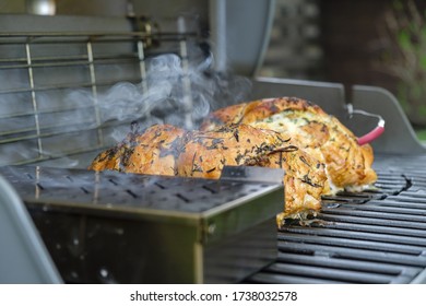 Large Chunks Of Meat Are Smoked On A Gas Grill. In The Foreground Is A Container For Wood Chips. Smoke Is Coming Out Of The Container.