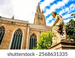 A large church with a statue of a woman on top of a pedestal. The statue is dressed in a white robe and is sitting on a stone base. The church is surrounded by trees and has a large window on the side