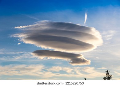 Large circular cloud forms (Altocumulus lenticularis duplicatus V-39) in the evening sky over Malaga city, Spain. Airplane trace in the sky on the background