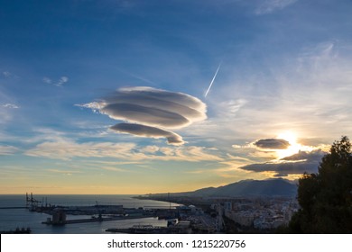 Large circular cloud forms (Altocumulus lenticularis duplicatus V-39) in the evening sky over Malaga city, Spain. Airplane trace in the sky on the background