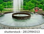 Large circular water diversion structure with a high fountain spraying water upward in a green public park.