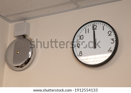 A large clock and a metal electronic bell on the wall for the signal of the beginning and end of classes in school, college, institute. The beginning and end of the shift of work in the company.