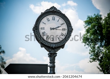 Large clock in the park with a signpost.