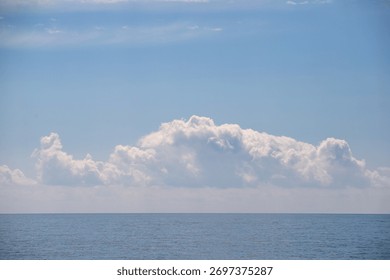 A large cloud is floating over the ocean. The sky is clear and blue, and the water is calm. The scene is peaceful and serene, with the cloud providing a sense of depth