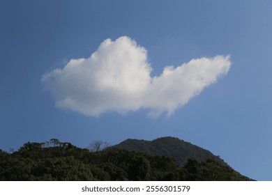 A large cloud is floating in the sky above a mountain. The sky is clear and blue, and the cloud is white and fluffy. Concept of calm and serenity