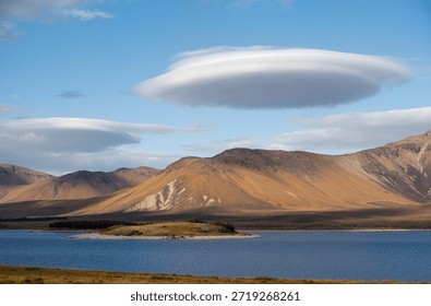 A large cloud hovering over a mountain range with a lake in the foregrounda
