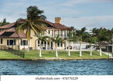 Large Coastal Home With A Small Boat Tied To Pier. Modern Luxury Waterfront Real Estate In Florida.