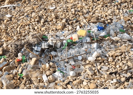 Large collection of discarded plastic bottles scattered across a pebbled riverbank, highlighting environmental pollution and waste mismanagement.