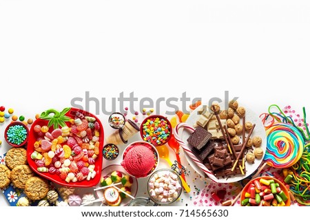 Large colorful selection of kids party food and sweets with cookies, ice cream, lollipops and candy isolated on white as a lower border with copy space