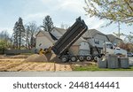 Large, commercial, dump truck unloading load of stone or gravel at construction site.