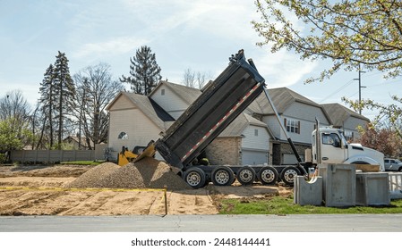 Large, commercial, dump truck unloading load of stone or gravel at construction site.