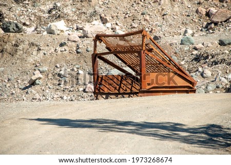 A large commercial topsoil screener for shifting and removing rocks from soil. The rusty metal sifter is in a construction site or quarry yard. The heavy machinery sits near large rocks and soil.