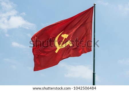 Large communist flag floating in the wind with a blue sky background