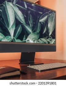 Large Computer Monitor With White Keyboard And Black Notebook On A Wooden Desk With Orange Warm Backlight 