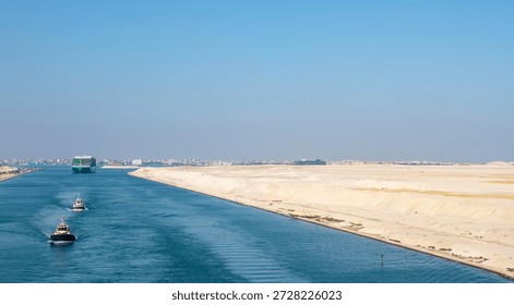 Large container ship, accompanied by tugboat, passing through the Suez Canal in Egypt.