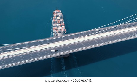 A large container ship sails under the YSS Cable Bridge. 300 meters long cargo vessel heading towards the Istanbul. Aerial Bosphorus Sea.
