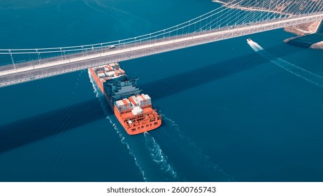 Large container ship sails under the YSS Cable Bridge. 300 meters long cargo vessel heading towards the Istanbul. Aerial Bosphorus Sea.