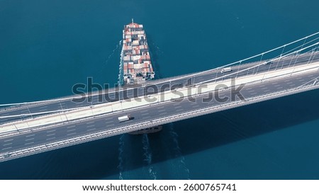 A large container ship sails under the YSS Cable Bridge. 300 meters long cargo vessel heading towards the Istanbul. Aerial Bosphorus Sea.