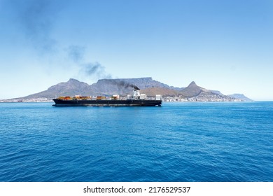 Large Container Ship At Sea In Front Of Cape Town And Table Mountain. Vessel Emitting Black Exhaust Smoke From Funnel. Air Pollution Concept.