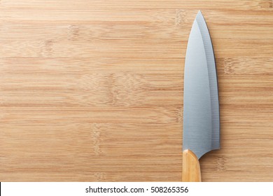 Large cooking (chefs) knife with a wooden handle in the right part of the vertical wooden cutting (chopping) board