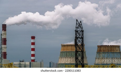 Large Cooling Towers Of Thermal Power Plants. White Steam Comes Out Of The Cooling Tower Against The Background Of The Sky With Clouds. Production Pipes And Cooling Towers.