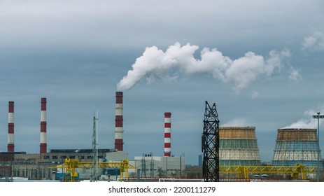 Large Cooling Towers Of Thermal Power Plants. White Steam Comes Out Of The Cooling Tower Against The Background Of The Sky With Clouds. Production Pipes And Cooling Towers.