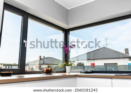 Large corner window in a modern kitchen with built-in cabinets against the wall with white fronts.