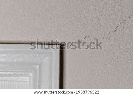 A large crack in the wall extends from the white frame of a doorway. 
