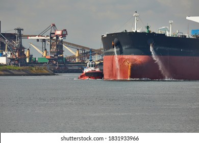 Large Crude Oil Tanker Ship Pumping Out Ballast Water When Coming Into Port In Rotterdam, Tug Boat Pushing The Side