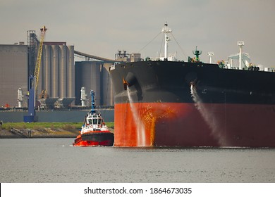 Large Crude Oil Tanker Ship Pumping Out Ballast Water When Coming Into Port In Rotterdam, Tug Boat Pushing The Side